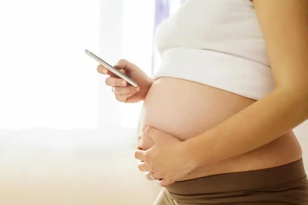 Woman holding a smartphone next to her pregnant belly