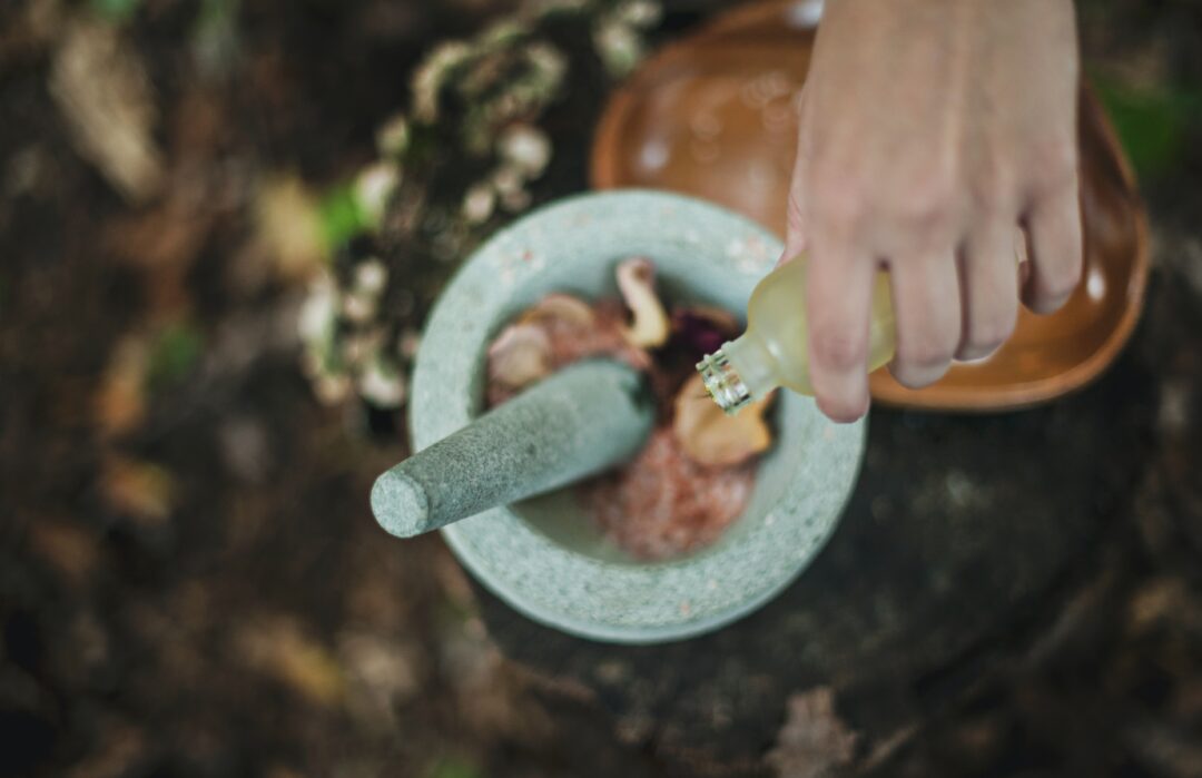 High angled photo of person pouring liquid from a bottle into a mortar containing herbs