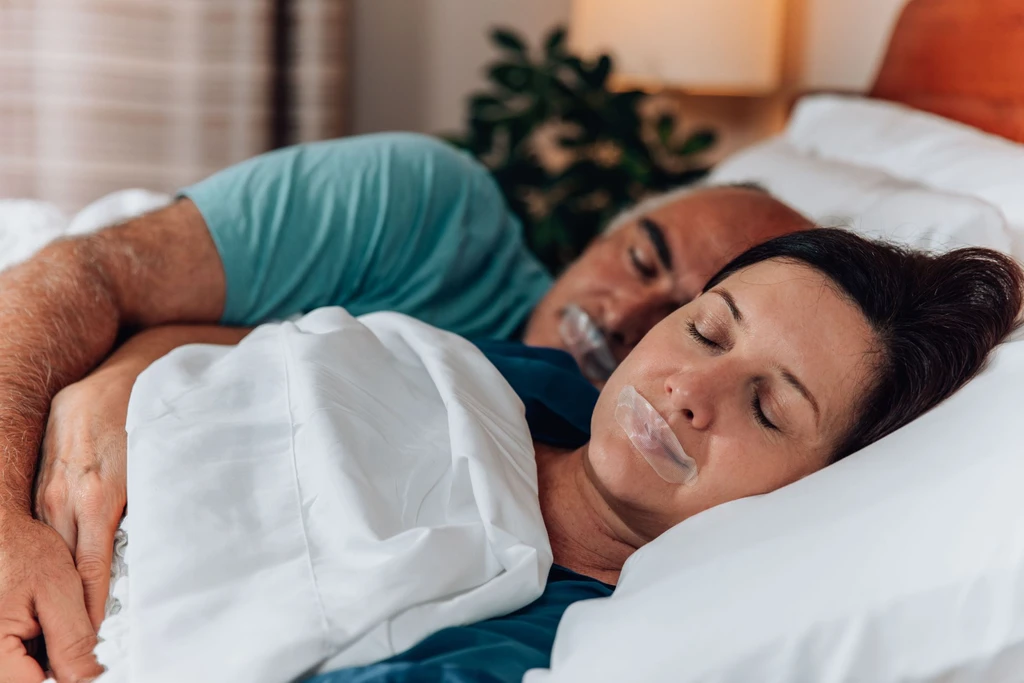 Couple sleeping in bed with their mouths taped